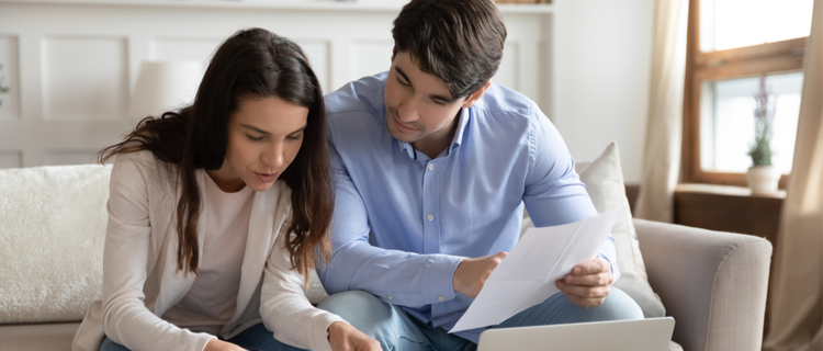 young couple sitting on sofa looking at financial paperwork