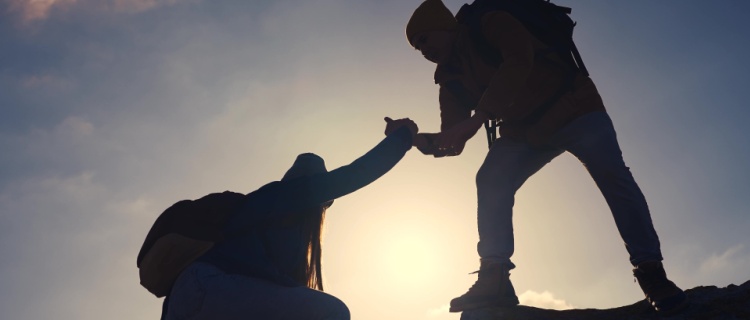 person helping another climber onto the summit of a mountain