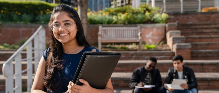 woman smiling holding a laptop in front of stairs