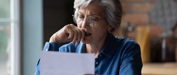 An older woman reading a letter, looking concerned