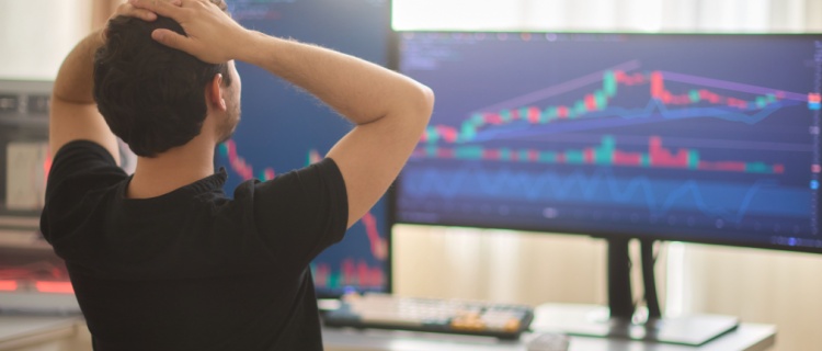 An investor with his head in his hands, looking at a screen