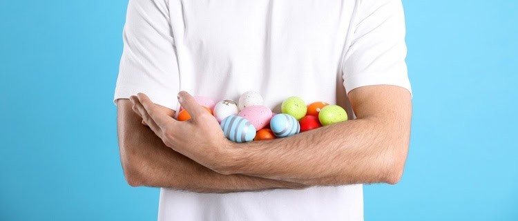 man in a white t-shirt holding a bundle of colourful eggs in his arms